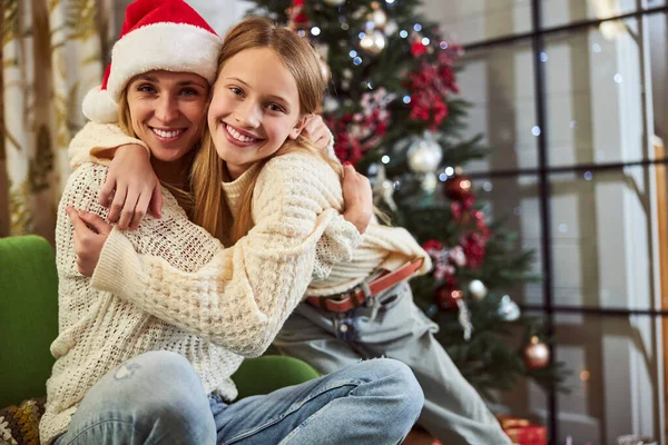 Chica alegre abrazándose con mamá en Navidad en el interior —  Fotos de Stock