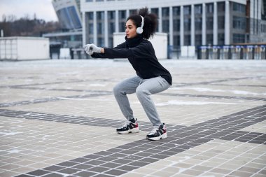 Meydanda çömelme hareketleri yapan konsantre bir sporcu.