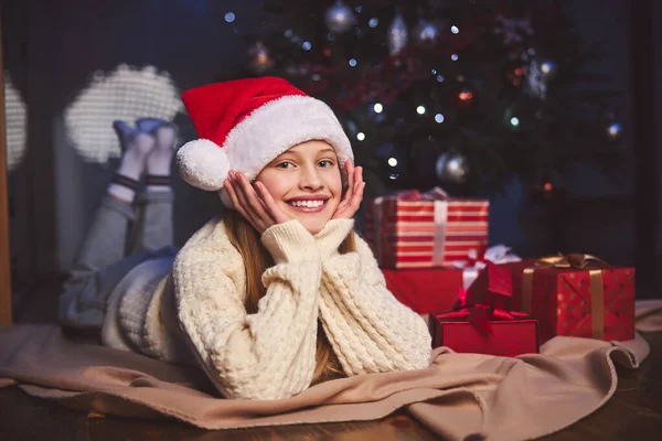 Feliz adolescente mujer relajándose cerca del árbol de Navidad en el interior —  Fotos de Stock