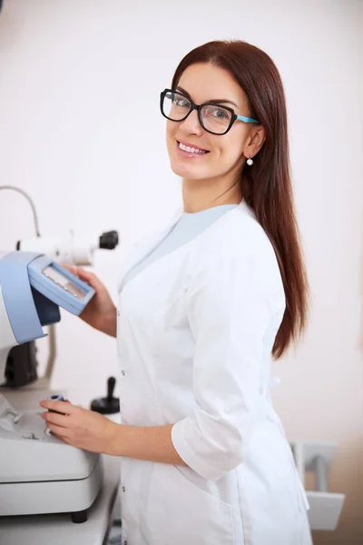 Красивый глазной врач улыбается во время работы авторефрактометра — стоковое фото