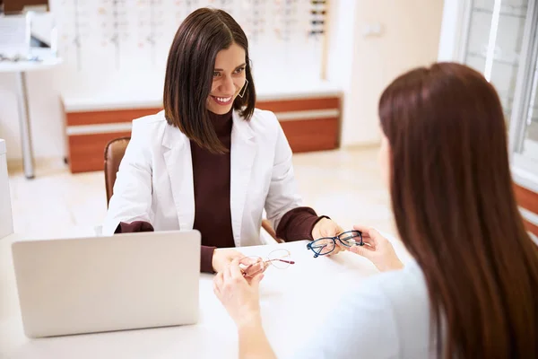 Óptico alegre mantener gafas por las sienes antes de la cara del cliente — Foto de Stock