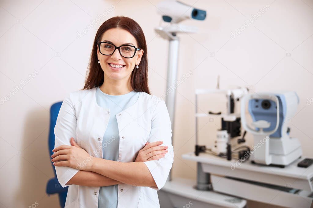 Happy ophthalmologist is standing near her equipment