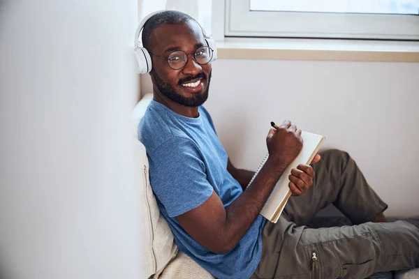Homem afro-americano satisfeito apoiado em um travesseiro com um bloco de notas — Fotografia de Stock
