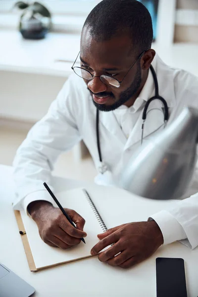 Profissional médico focado está escrevendo em óculos — Fotografia de Stock