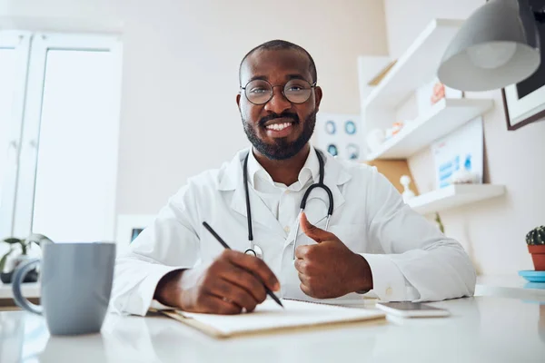 Persona médica multiétnica con un lápiz que da pulgares hacia arriba — Foto de Stock