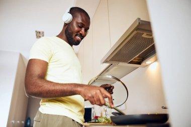 Erkek bir tavayı açar ve içindeki yemekleri karıştırır.