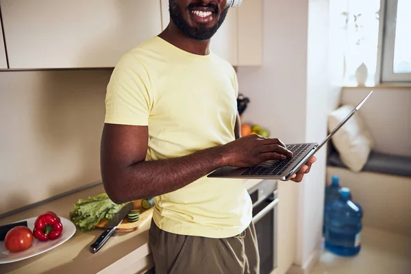 Hombre adulto presionando las teclas en el portátil cerca de una mesa de cocina —  Fotos de Stock