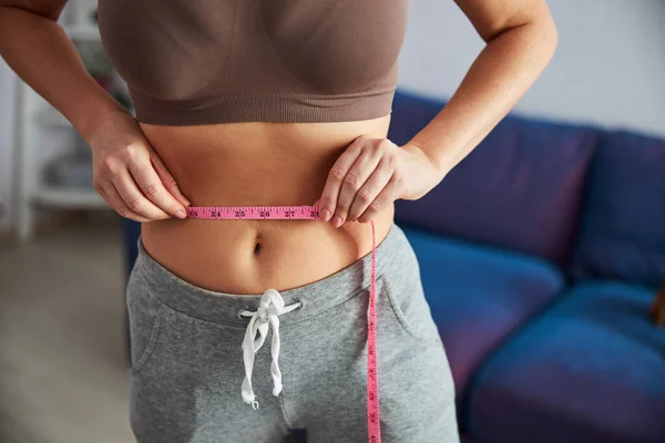 Woman checking waist size in living room — Stock Photo, Image