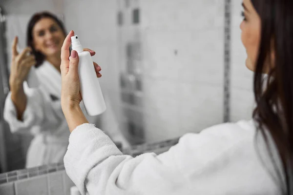 Femme souriante utilisant un spray cosmétique à la maison — Photo