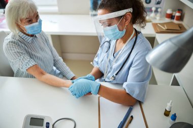 Deneyimli doktor yaşlı bir kadının nabzını kontrol ediyor.