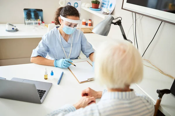 Dokter schrijft in haar notitieboekje voor een oudere patiënt — Stockfoto