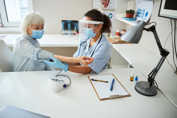 Doctor putting on a pressure cuff to a pensioner arm — Stock Photo, Image