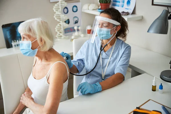 Medico con uno stetoscopio che sente una vecchia signora respirare — Foto Stock