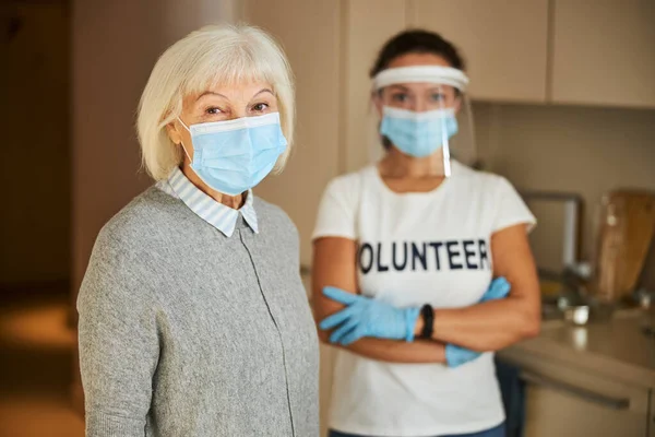 Freiwillige in Latexhandschuhen stehen hinter einer Seniorin — Stockfoto