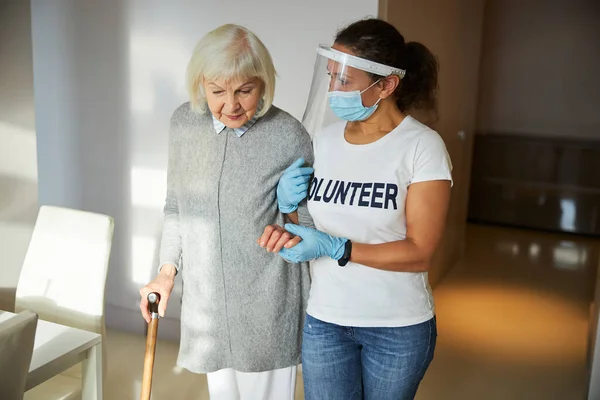 Опекун в латексных перчатках помогает пенсионеру ходить — стоковое фото