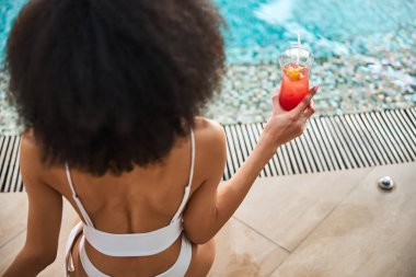 Muhteşem saçlı genç bayan havuz kenarında içeceklerin tadını çıkarıyor.