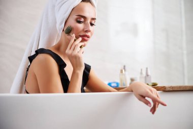 Rahatlamış bir kadın cildine özel bir silindirle masaj yapıyor.