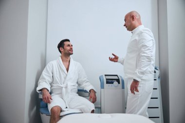 Hastanede doktorla konuşan neşeli bir adam.