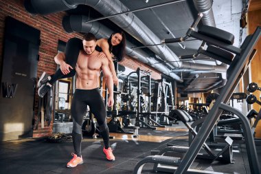 Antrenman sırasında kız arkadaşını omuzlarında taşıyan güçlü bir vücut geliştirici.