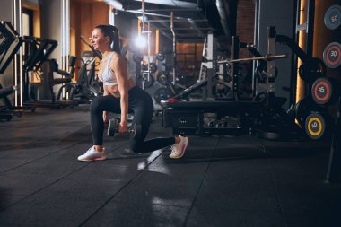 Neşeli genç bir kadın ağırlıklarla hamle yapıyor.