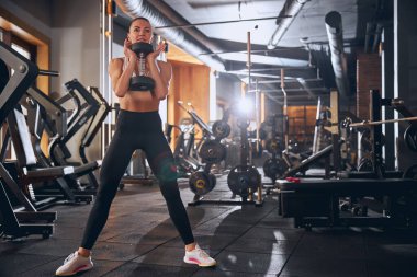 Spor salonunda kalça egzersizi yaparken neşeli genç bir kadın.