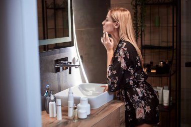 Banyodaki aynada yüzünü kontrol eden kadın.