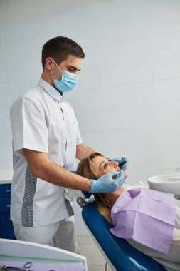 Muayene sırasında dişçi koltuğunda oturan bir hastanın arkasında duran dişçi.