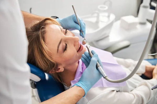 Médico cuidando de los dientes de la señora tranquila con la máquina de perforación — Foto de Stock