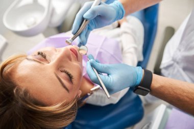 Diş hekimi ağız için ayna ve matkap tutuyor.