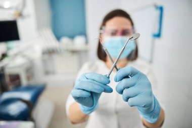 Tıbbî görevliler birbirlerine diş aynası ve sonda gösteriyorlar.