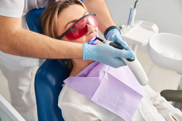 Dentist employing dental curing light on a woman patient