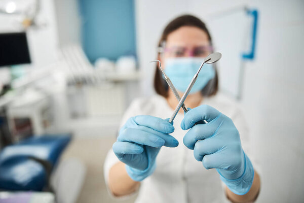 Medical worker showing dental mirror and probe across each other