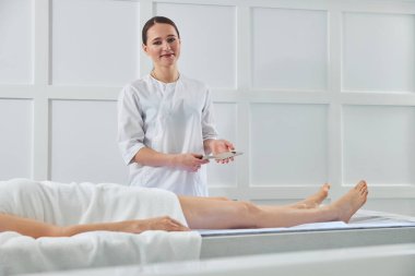 Yakışıklı masöz müşterinin yanında duruyor ve elinde metal bir alet tutuyor.