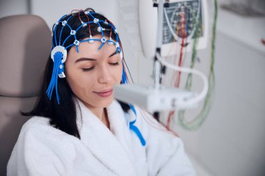 Koyu renk saçlı kadın hasta elektroansefalografi görüyor.