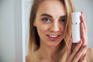 Gülümseyen kadın iki eliyle nemlendirici tutuyor.