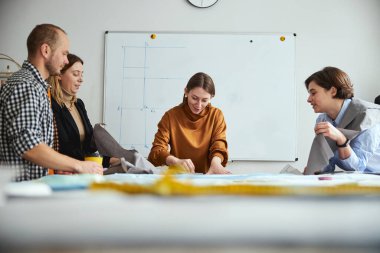 Grup arkadaşları terzilik öğrencilerinin kumaş taslaklarını izliyorlar.