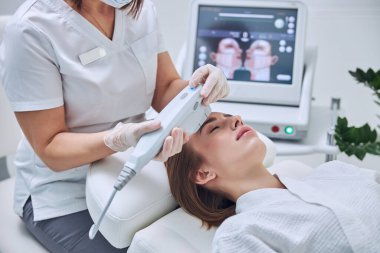 Kızıl saçlı beyaz kadın kozmetoloji merkezinde deri tedavisinde vakit geçiriyor.