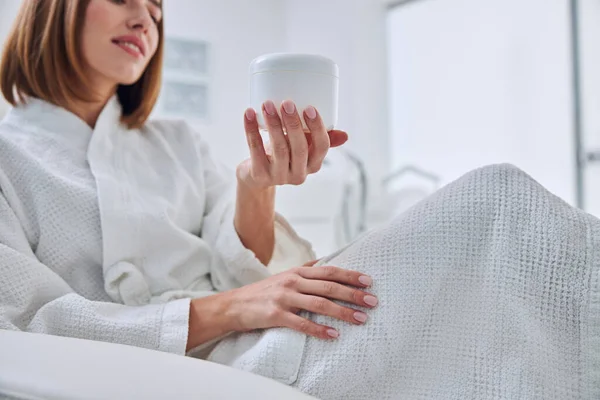 Charming young female sitting in the cosmetologist cabinet and choosing care product — Stock Photo, Image