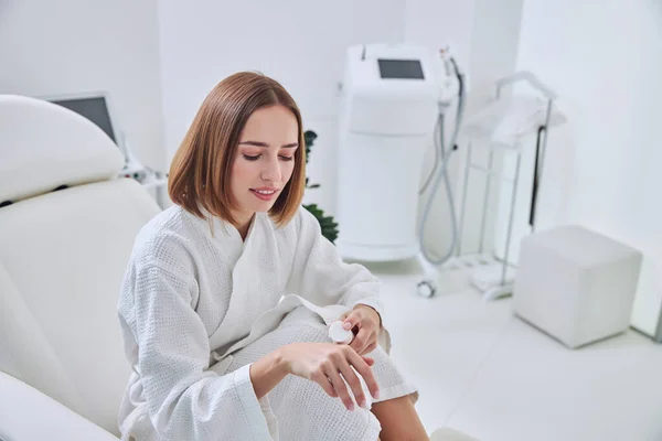 Gyönyörű fiatal nő ül az orvosi széken, miközben vigyáz a bőr a kezét a kozmetikai klinikán — Stock Fotó