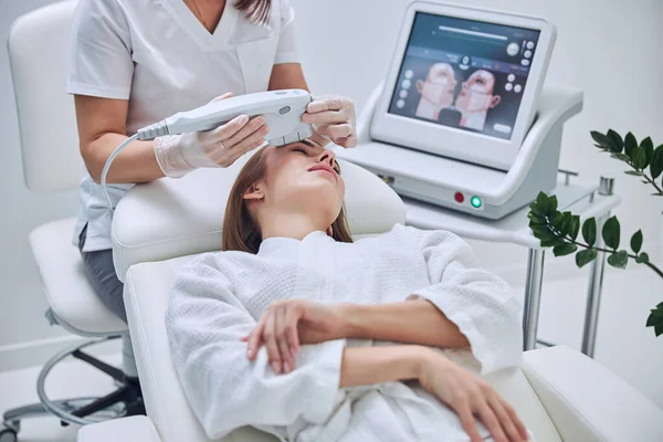 Happy beautiful female client receiving professional vacuum face massage in medicine clinic — Stock Photo, Image