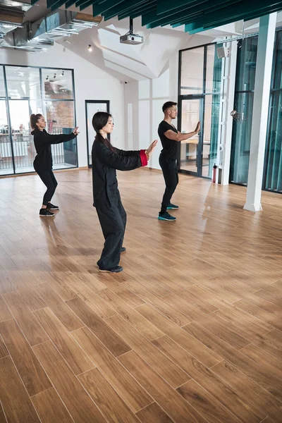 Pessoas ligeiramente dobrável joelhos enquanto esticar os braços durante tai chi — Fotografia de Stock