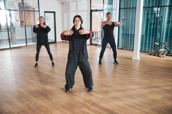 Dos mujeres y un hombre deportivo usando la forma de tai chi —  Fotos de Stock