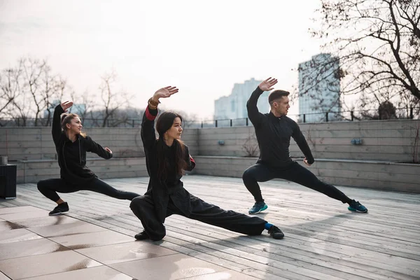Três pessoas fazendo tai chi deep side lunge — Fotografia de Stock