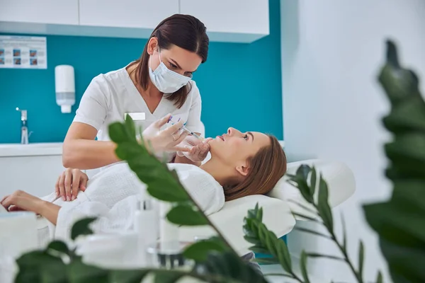 Elegante hübsche Frau im weißen Bademantel erhält Anti-Aging-Biorevitalisierung in Kosmetikzentrum — Stockfoto