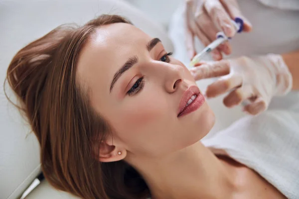 Focused adorable Caucasian woman lying on medicine chair while receiving anti aging biorevitalization in spa salon — Stock Photo, Image