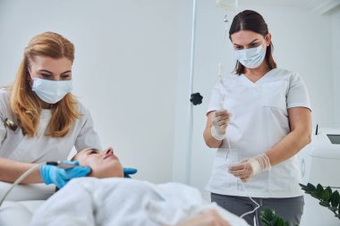 Seriously two physicians working with female client in beauty clinic