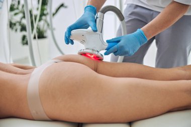 Unrecognized lady lying on medicine table while getting anti-fat treatment in spa salon