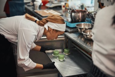 Skillful pastry chef inserting tray with desserts into oven