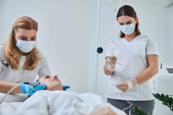 Seriously two physicians working with female client in beauty clinic — Stok fotoğraf