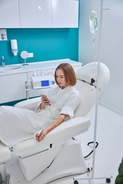 Adorable elegant Caucasian female sitting in medicine armchair during medical procedure in spa salon — Stok fotoğraf